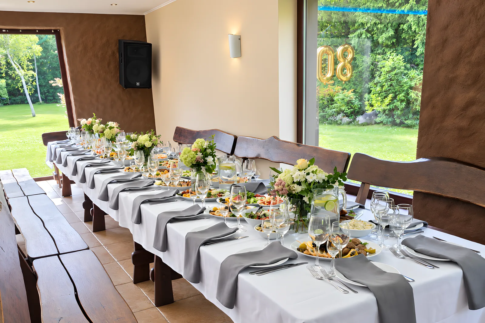The hall laid for a celebration: a long table with flowers and glasses, birches and a meadow beyond the glass wall