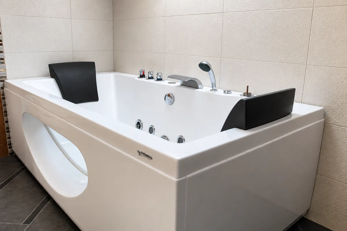 A white jacuzzi bath with black headrests, chrome taps and massage jets